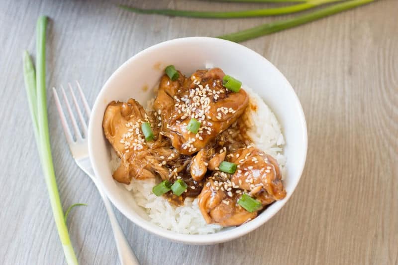 A bowl of Instant Pot Sesame Chicken topped with sesame seeds and garnished with chopped green onions.