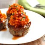 Two meatloaf sweet potato muffins topped with mashed sweet potato and garnished with parsley, served on a white plate with a fork on the side.