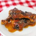 Crock Pot Sticky Asian Chicken Legs on a white plate with a red and white checkered tablecloth.