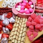 A Valentine's Day Charcuterie Board featuring an assortment of themed candies and cookies on a wooden board.