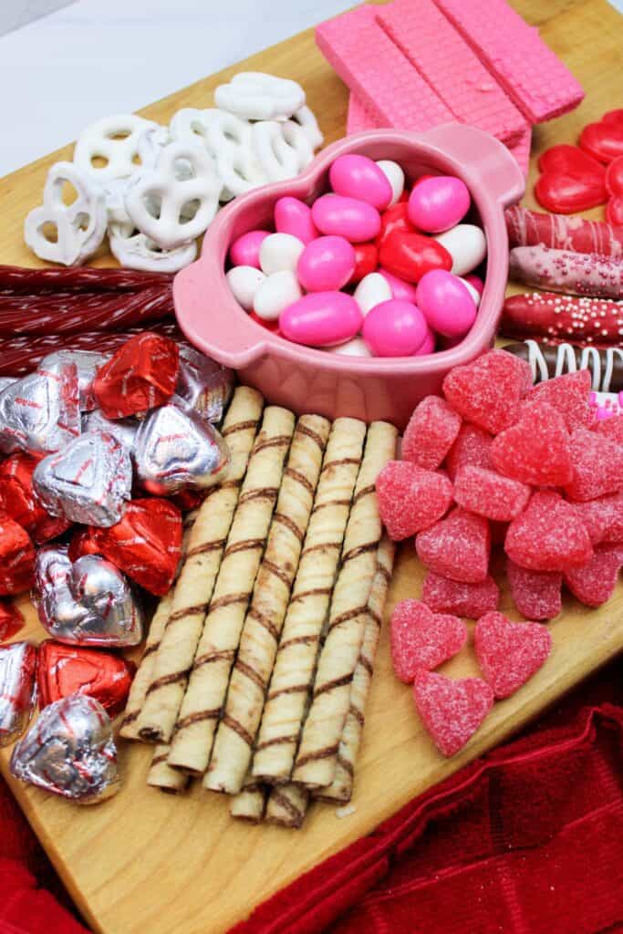 A Valentine's Day Charcuterie Board featuring an assortment of themed candies and cookies on a wooden board.