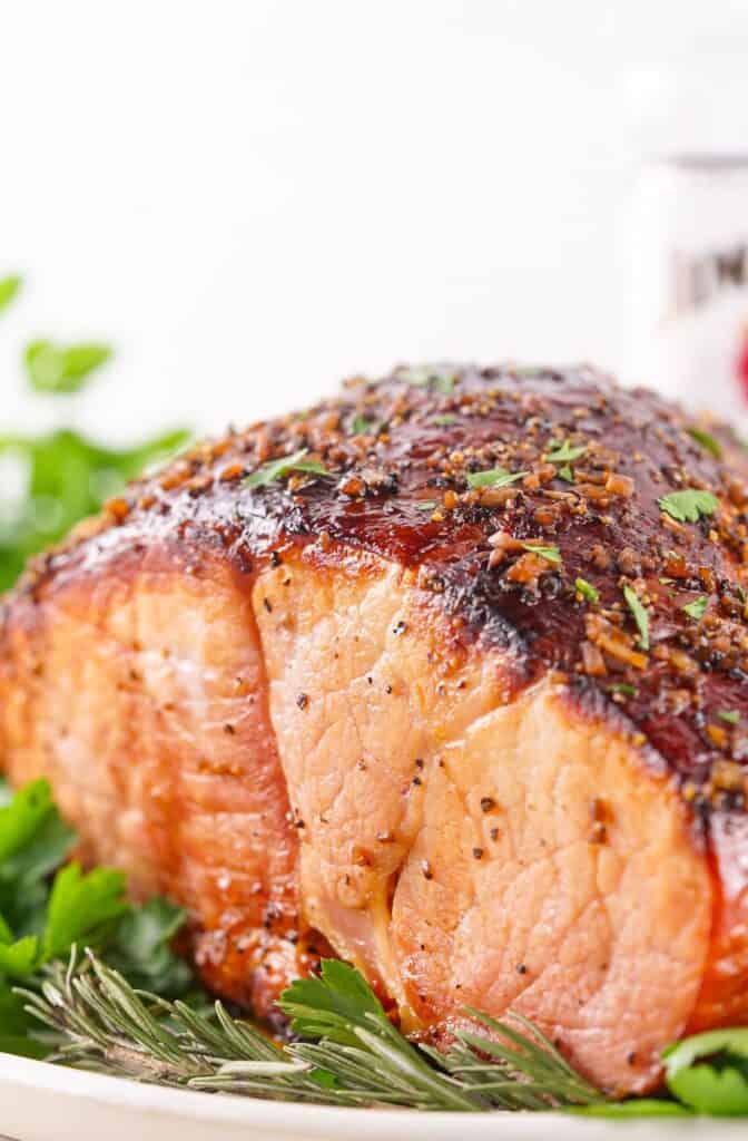 A close-up image of a seasoned, bourbon glazed ham garnished with herbs.