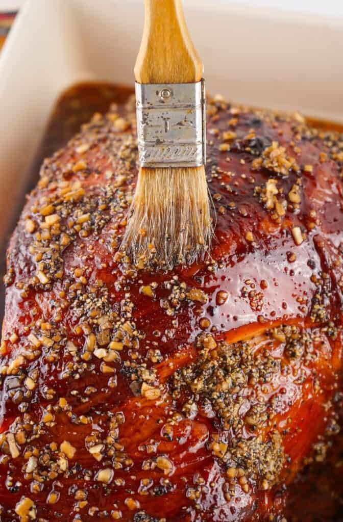 Glazing a roasted Bourbon Glazed Ham with a brush sprinkled with seasoning.