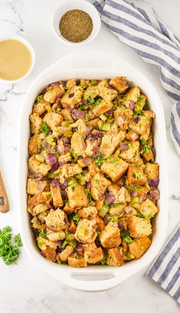 A casserole dish filled with Traeger Smoked Stuffing, garnished with herbs and surrounded by ingredients.