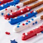 Firecracker Pretzel Rods coated with red, white, and blue chocolate and decorated with star-shaped sprinkles are arranged on a white surface, making them the perfect easy party snacks.