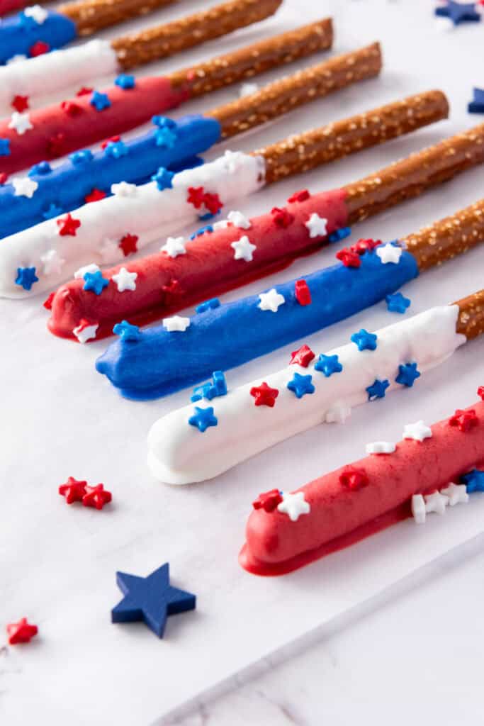 Firecracker Pretzel Rods coated with red, white, and blue chocolate and decorated with star-shaped sprinkles are arranged on a white surface, making them the perfect easy party snacks.