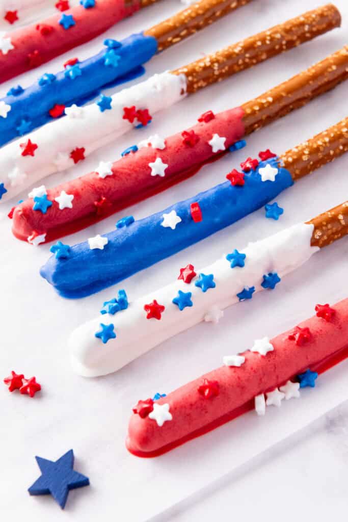 Firecracker Pretzel Rods coated in red, white, and blue chocolate with star-shaped sprinkles lie in rows on a white background, making them the perfect patriotic snacks.