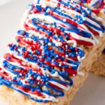These Independence Rice Krispie Treats are adorned with vibrant red, white, and blue icing and sprinkles, elegantly displayed on a pristine white surface.