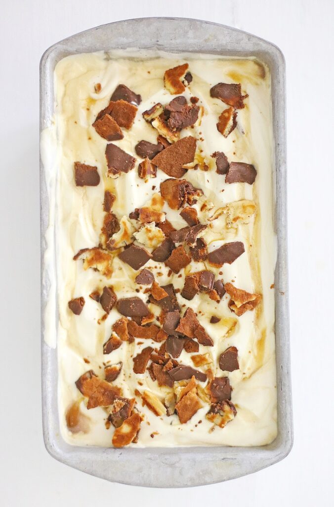 A rectangular metal container brims with creamy vanilla ice cream, lavishly topped with brown cookie or chocolate pieces, capturing the essence of Ben & Jerry’s Copycat No Churn Homemade Americone Dream Ice Cream.