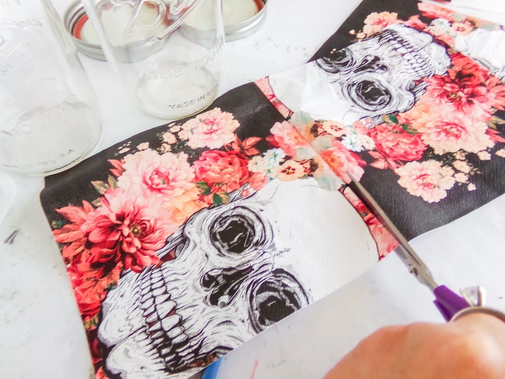 Skull Cookie Mix in a Jar 6 A person cuts floral skull-patterned paper next to glass jars on a white surface.