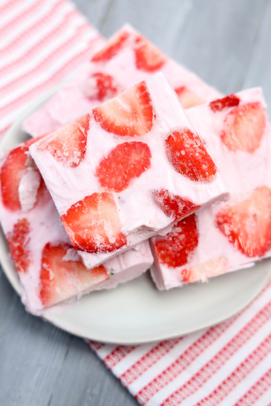 Plates with strawberry frozen yogurt bark squares sit on a striped cloth background.