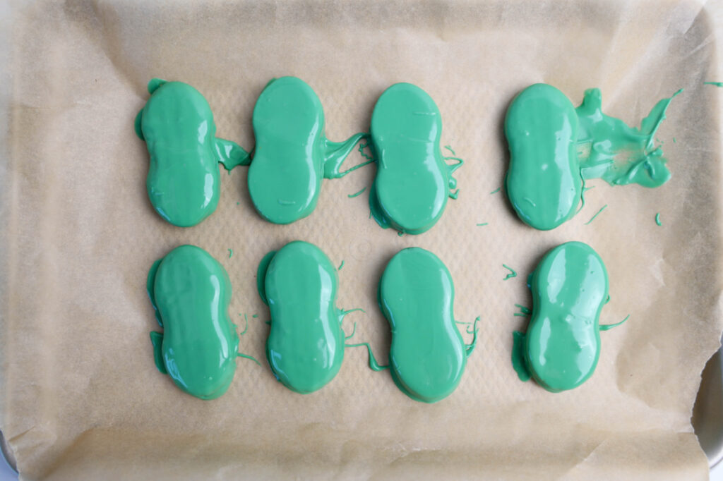 Eight green candy shapes, reminiscent of Mardi Gras Alligator Cookies, rest neatly on a parchment-lined baking tray.