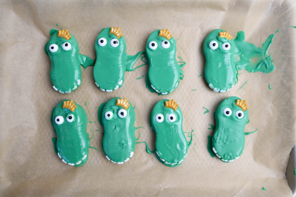 Eight delightful green, Mardi Gras Alligator Cookies with candy eyes and gold sprinkles shimmer on parchment paper, perfectly capturing the festivity's vibrant spirit.