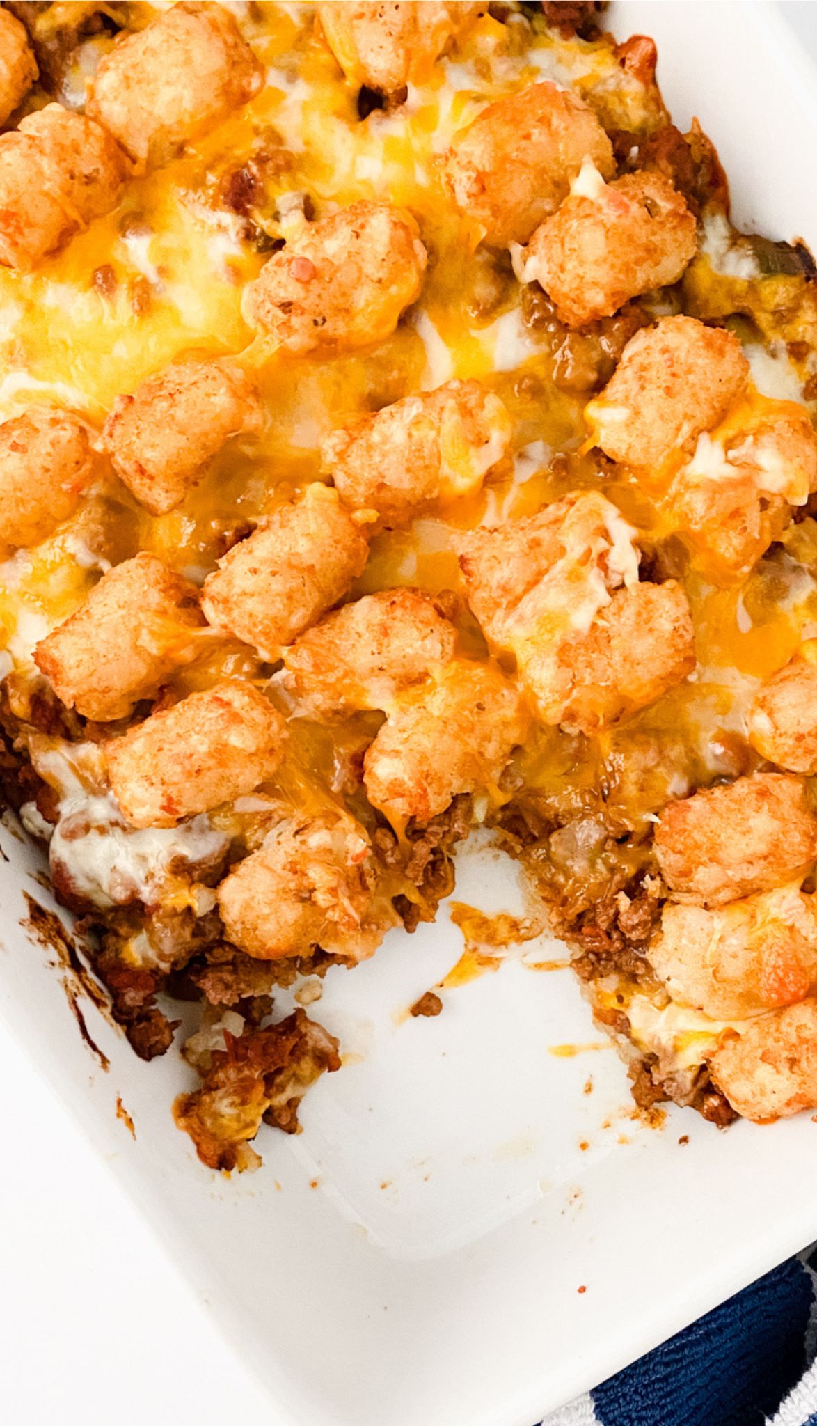 A Taco Tot Casserole dish brimming with ground meat, melted cheese, and a topping of golden-brown tater tots sits invitingly, a tempting portion already missing.