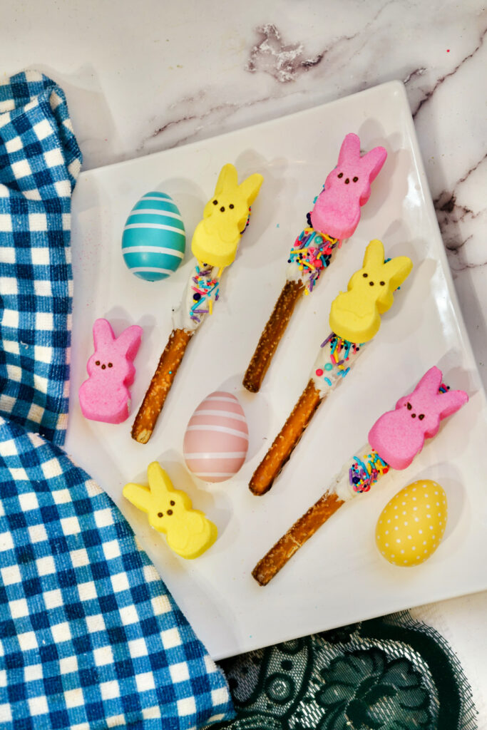 Peeps Pretzel Rods 8 Colorful marshmallow bunnies and pastel eggs on a plate are complemented by Peeps Pretzel Rods, decorated with white chocolate and sprinkles, next to a blue checkered cloth.