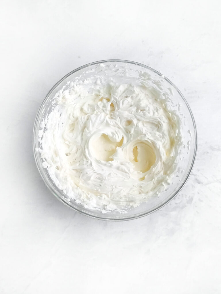 Tiramisu Easter Bunny – A Fun Twist on the Classic Italian Dessert 5 A glass bowl filled with fluffy, white whipped cream sits on a white surface, resembling the soft tail of an Easter Bunny.