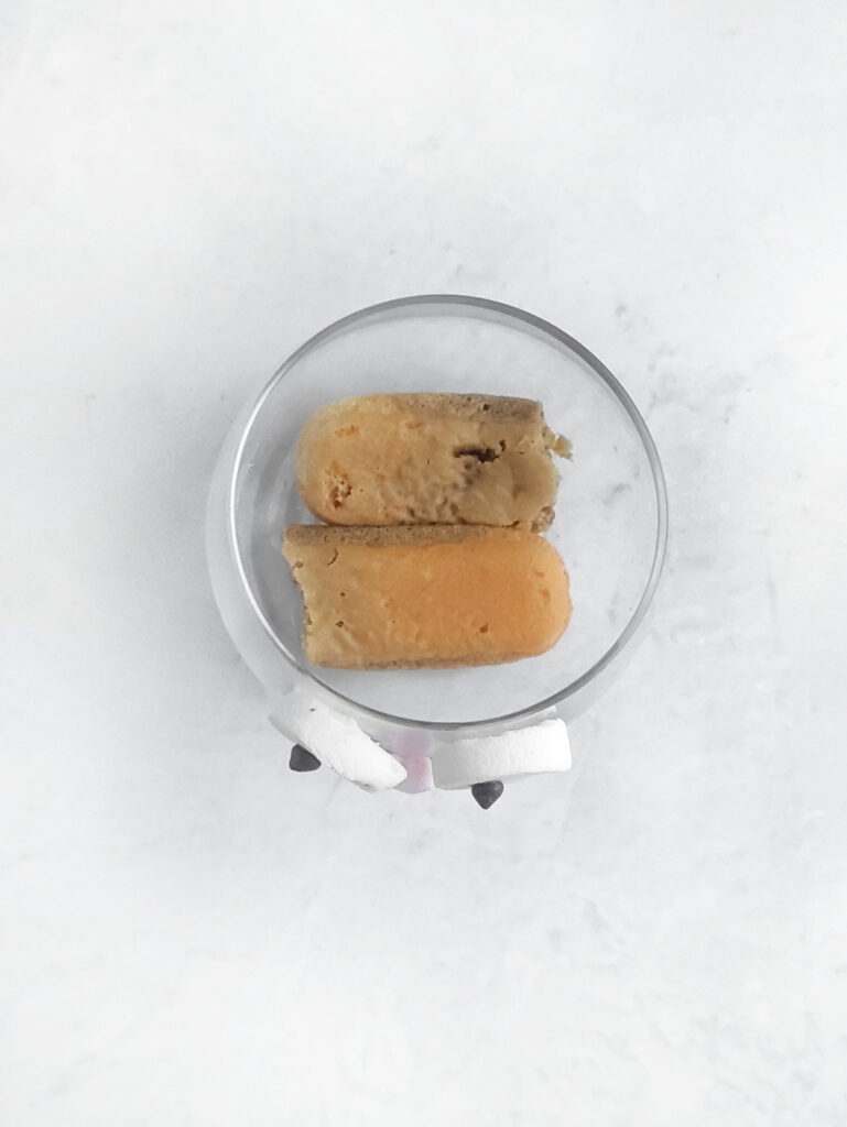 Tiramisu Easter Bunny – A Fun Twist on the Classic Italian Dessert 6 Two pieces of tiramisu, one partially eaten, rest in a small glass dish on a white surface. The layers resemble the soft fluff of an Easter Bunny, inviting and delightful from top view.