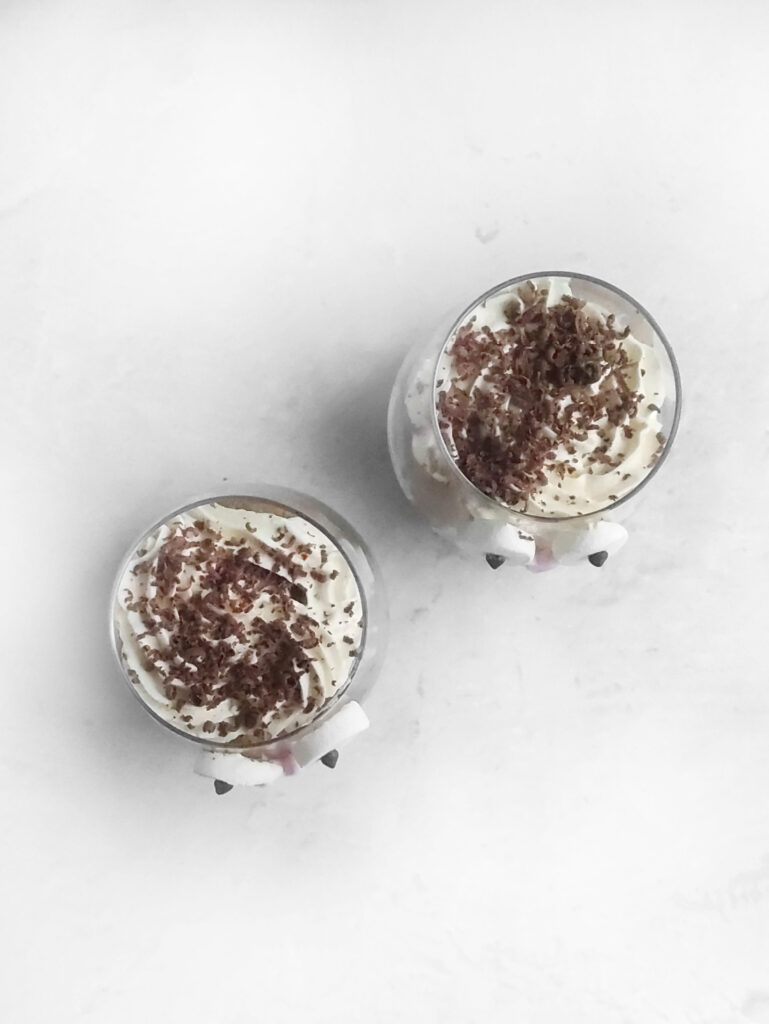 Tiramisu Easter Bunny – A Fun Twist on the Classic Italian Dessert 8 Two glasses filled with a creamy tiramisu dessert topped with chocolate shavings, viewed from above on a white surface.