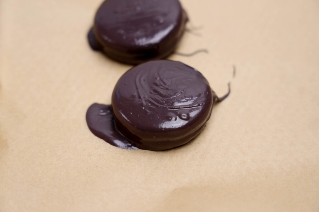 Summerween Slasher Oreos 6 Two round Summerween Slasher Oreos rest on a sheet of brown parchment paper, with some chocolate pooled around the edges.