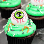 Spooky Halloween Eyeball Cupcakes: The Perfect Creepy-Cute Treats 11 Chocolate cupcake with bright green frosting, colorful sprinkles, and a large, realistic candy eyeball on top—perfect for Spooky Halloween Eyeball Cupcakes displayed on a dark surface.