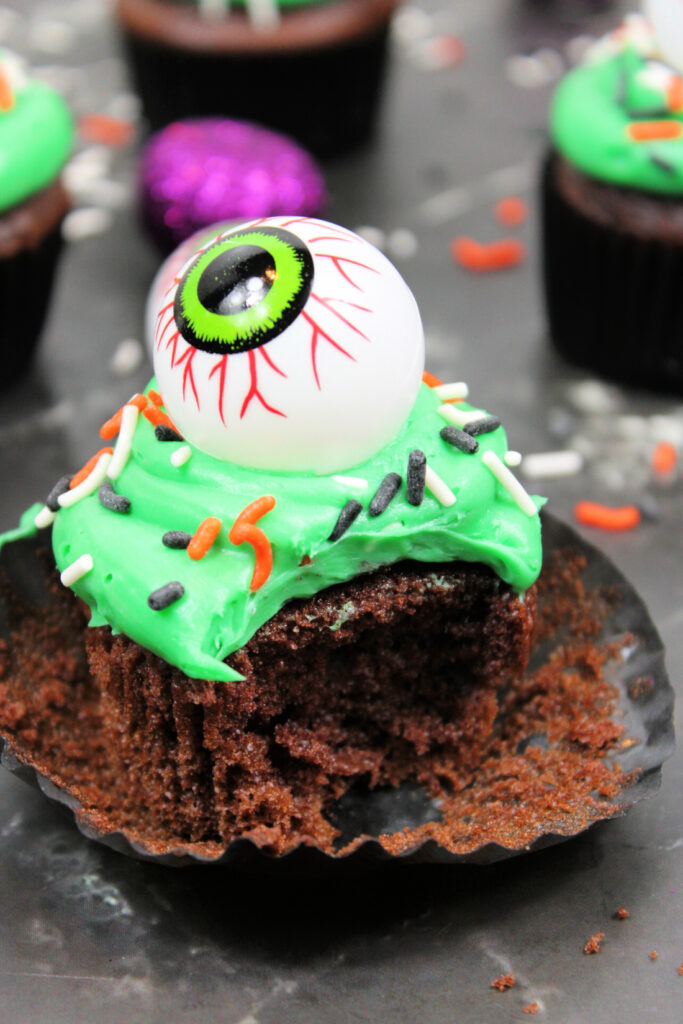 Spooky Halloween Eyeball Cupcakes: The Perfect Creepy-Cute Treats 8 Partially eaten and unwrapped, this Spooky Halloween Eyeball Cupcake features chocolate cake, green frosting, festive sprinkles, and a creepy plastic eyeball topper for the perfect eerie treat.